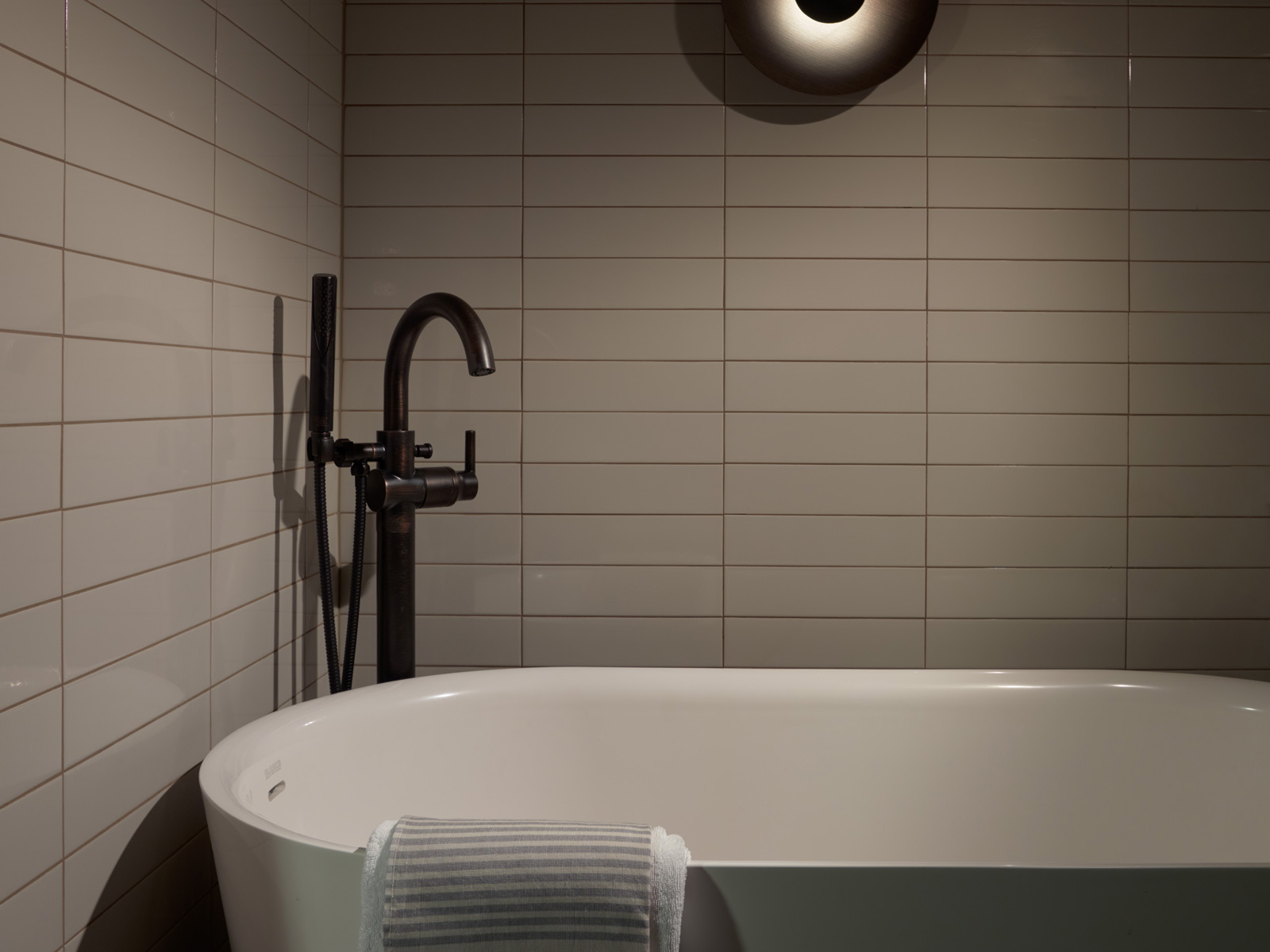 Large soaking tub with modern gray subway tile and circular light fixture