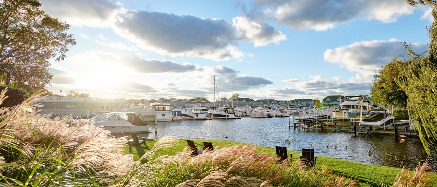 View of the New Buffalo harbor at sunset from the Harbor Grand Hotel. Tall summer grasses with Adirondack chairs facing the water with boats