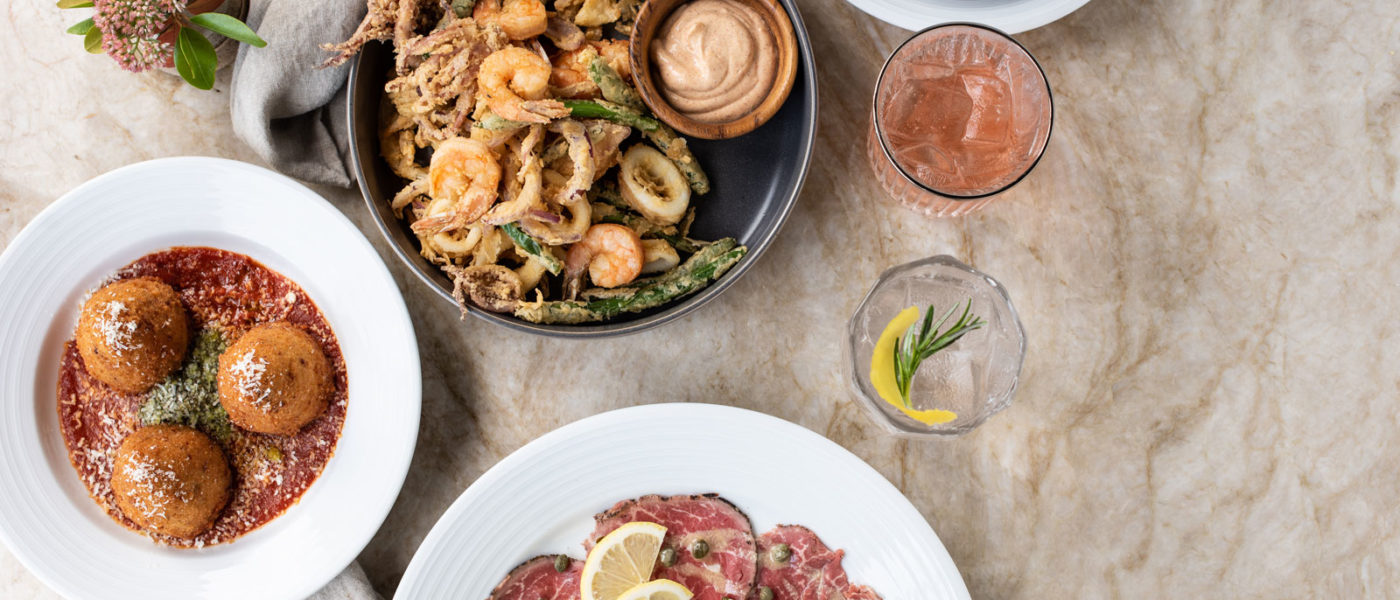 Top-down view of a marble table with shrimp scampi al forno, beef carpaccio, arancini, and fritto misto