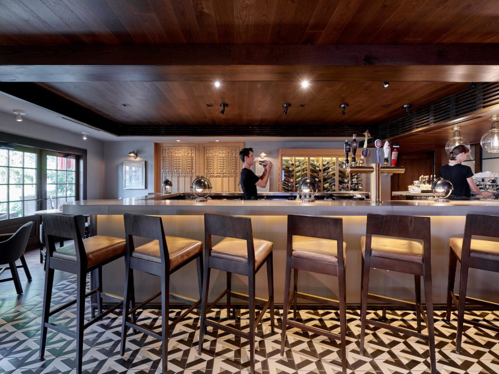 U-shaped bar with graphic tile flooring, wooden barstools, and two bartenders preparing drinks