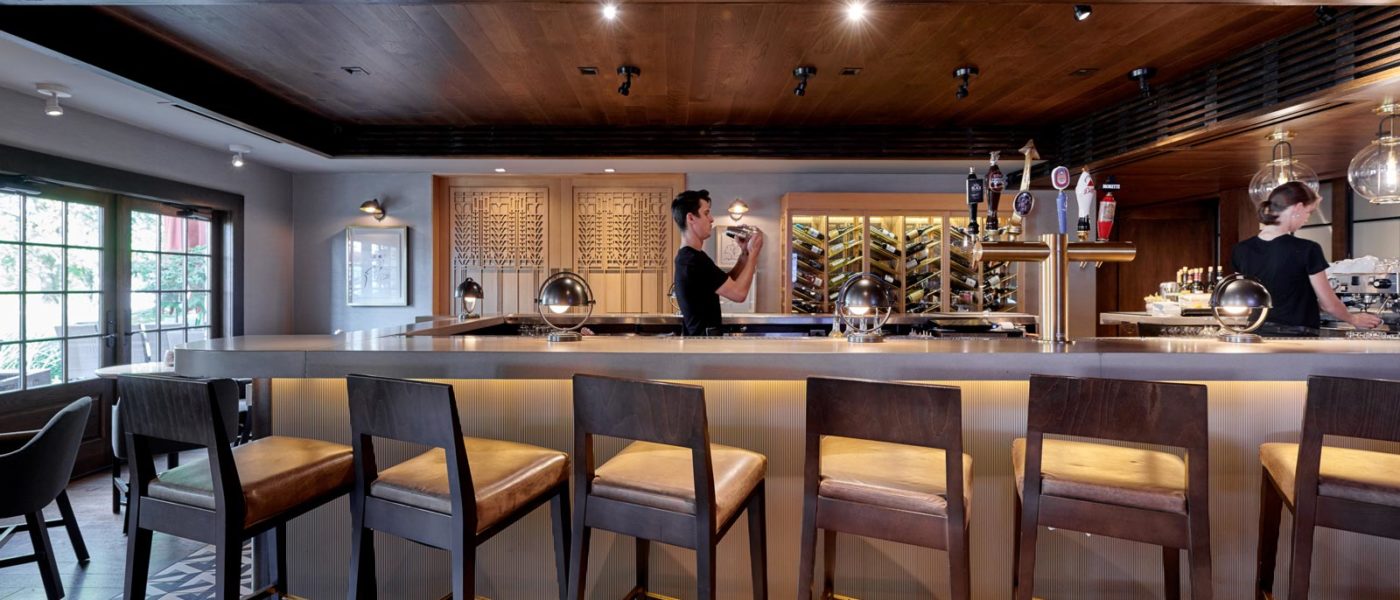 U-shaped bar with graphic tile flooring, wooden barstools, and two bartenders preparing drinks