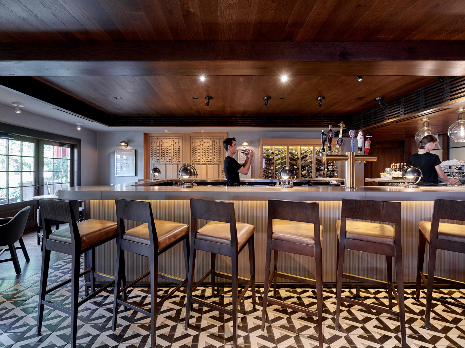 U-shaped bar with graphic tile flooring, wooden barstools, and two bartenders preparing drinks