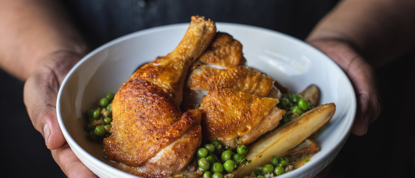 Chef holding a bowl of crispy, golden brown chicken with potatoes and peas