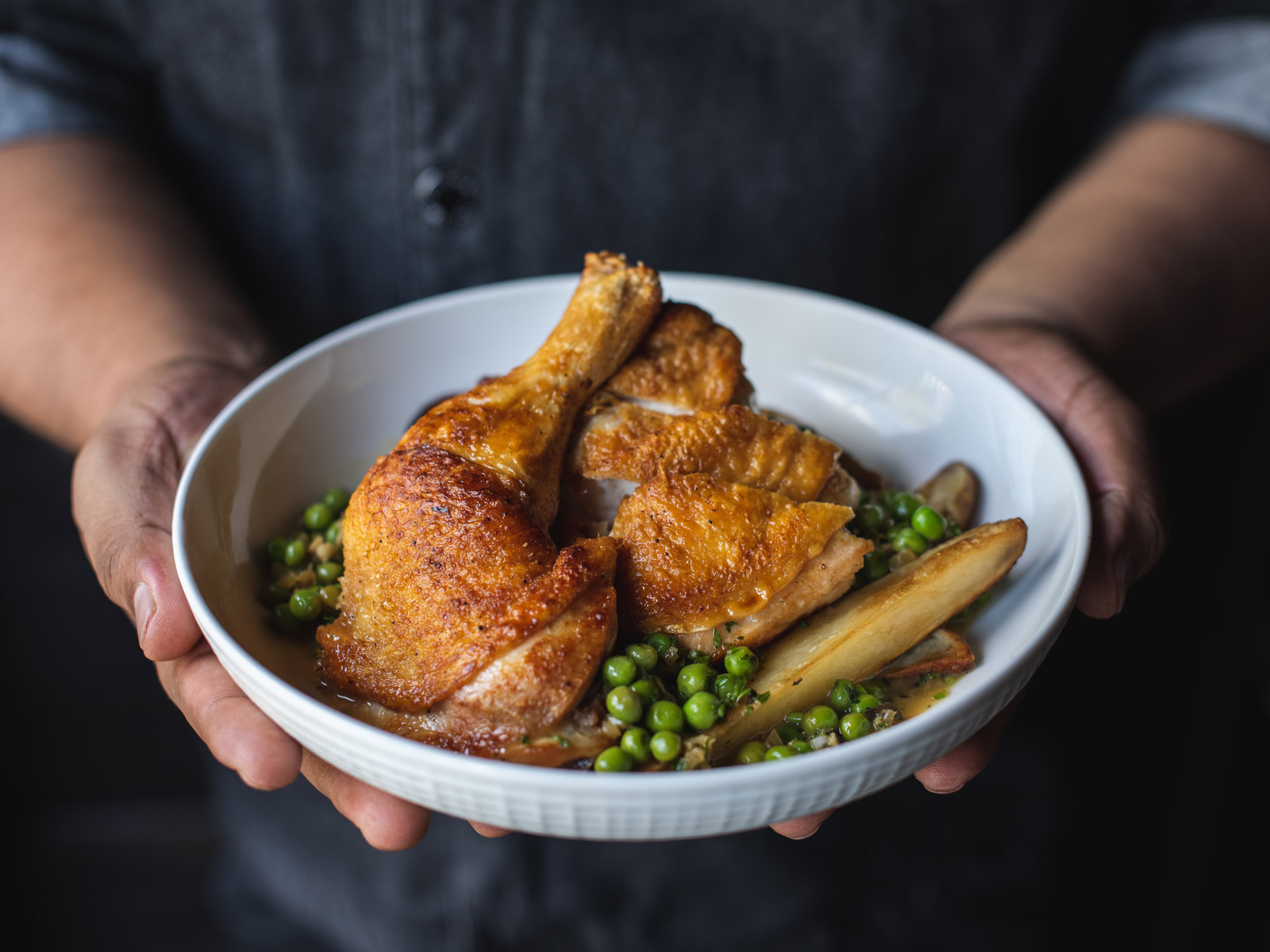 Chef holding a bowl of crispy, golden brown chicken with potatoes and peas