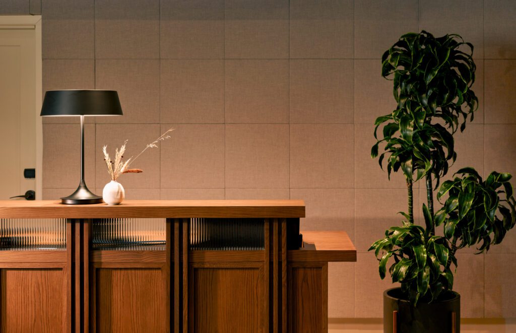wooden reception desk with a lamp, a vase with dry flowers and a big potted plant next to it at Harbor Grand Hotel